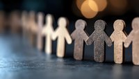 Wooden figures holding hands in line symbolizing unity, teamwork and community support against blurred warm bokeh background on dark surface.
