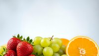 Fresh colorful fruits including strawberries, green grapes and orange slice arranged on clean white background for healthy eating concepts.