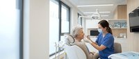 Female dentist in blue scrubs examining elderly male patient in modern dental office with advanced equipment and natural lighting.
