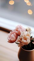 Delicate pink peonies in brown ceramic vase against soft bokeh lights background, creating romantic mood for wedding and home decor styling.