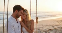 Romantic couple sharing intimate moment on beach swing at golden hour sunset, love and connection by ocean waves for wedding anniversary celebration.