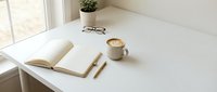 Minimalist workspace with open notebook, pen, coffee cup, eyeglasses, and potted plant on white desk by window for creative work and productivity.