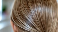 Smooth blonde hair strands in close-up view showing natural shine and healthy texture against blurred background, demonstrating professional hair care and styling results.