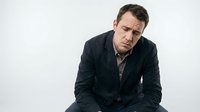 Stressed middle-aged Caucasian businessman in dark suit sitting with head in hands showing depression, anxiety and mental health struggles at workplace.