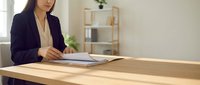 Professional Asian businesswoman reviewing documents at wooden desk in modern office workspace for corporate presentations and business meetings.