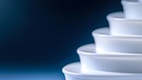 Minimalist composition of white ceramic bowls stacked in descending order creating geometric pattern with soft shadows against dark blue background.