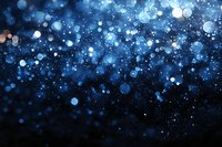 Glowing blue bokeh lights and particles floating on dark background create magical atmosphere for festive designs and holiday backgrounds.