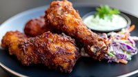 Crispy fried chicken wings glazed with spicy sauce, served on black plate with creamy dip and fresh coleslaw garnish. For restaurant menu and food photography.