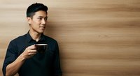Young Asian man in black shirt holding empty wallet against wooden wall background, depicting financial hardship and money problems.