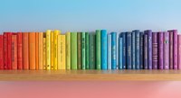 Colorful rainbow books arranged on wooden shelf creating vibrant spectrum from red to purple for education and learning concepts.