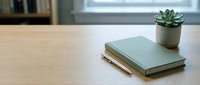 Minimalist workspace with green notebook, golden pen and small succulent plant on wooden desk surface creating calm productive environment for writing and planning.