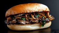 Gourmet mushroom sandwich with sautéed fungi and fresh herbs on artisan bun against dark background for culinary marketing and restaurant menu design.