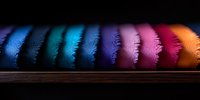 Colorful feather-like pattern in rainbow spectrum arranged in row on dark wooden surface creates dramatic lighting effect and vibrant texture display.