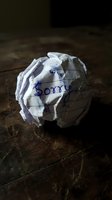 Crumpled paper ball with the word Sorry written in blue pen on a wooden surface, conveying regret, apology, and emotional conflict.