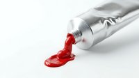 Red paint squeezed from silver tube onto white surface creating artistic splash for creative projects and design work.