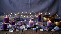 Purple candles burning among healing crystals, gemstones and singing bowl create mystical meditation atmosphere with warm fairy lights on wooden surface.