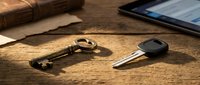 Antique brass key and modern car key fob on wooden desk surface with leather journal and digital tablet, representing security and access concepts.