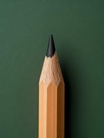 Sharp graphite pencil tip against green chalkboard background, macro close-up view showing wood texture and precise point for education and creativity concepts.