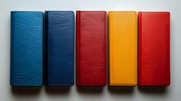 Colorful leather wallets arranged in row showing texture and variety of blue, navy, burgundy, yellow and red. Clean minimal composition on gray background.