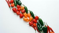 Fresh colorful chili peppers arranged in diagonal line on white background. Hot spicy vegetables for cooking, seasoning and culinary ingredients.