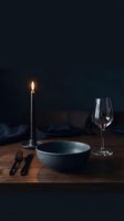 Elegant table setting with lit candle, empty bowl, wine glass and cutlery on wooden surface against dark background for fine dining and restaurant concepts.