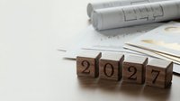Wooden blocks spelling 2027 on a desk with blueprints and documents, symbolizing future planning and business goals.