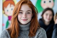 Young redhead woman with freckles wearing gray turtleneck sweater smiling at camera, natural beauty portrait with soft blurred background.
