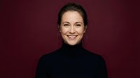 Professional Caucasian businesswoman in black turtleneck smiling confidently against burgundy background for corporate marketing and business presentations.