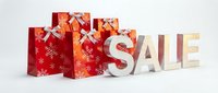 Red holiday shopping bags with snowflake patterns and silver bows arranged beside festive sale letters on white background for seasonal promotions.