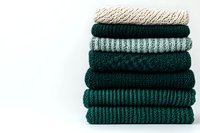 Stack of folded knitted sweaters in green and beige tones on white background, cozy autumn winter wardrobe concept.