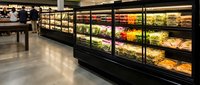 Modern grocery store produce section with fresh vegetables and fruits displayed in refrigerated cases with LED lighting for retail shopping experience.