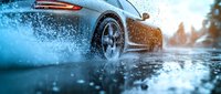 Luxury sports car driving through water puddle creating dramatic splash effect during sunset with atmospheric lighting.