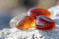 Translucent amber stones on rough surface in sunlight with natural bokeh background, glowing honey-colored minerals with smooth polished texture.
