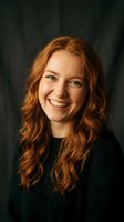Young Caucasian woman with curly red hair smiling warmly in dark green sweater against emerald background for lifestyle and portrait photography.