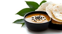 Traditional Indian dal lentil soup with black mustard seeds in ceramic bowl served with naan flatbread and curry leaves on white background.