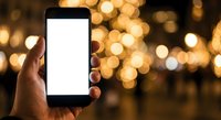 Hand holding smartphone with blank white screen against warm golden bokeh lights background for mobile app mockup and digital display presentation.