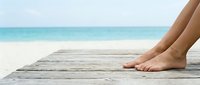 Woman's bare feet resting on wooden pier overlooking turquoise ocean and sandy beach, perfect for travel, vacation, and relaxation concepts.