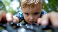 Young child with curious expression peering closely at something while exploring outdoors in nature, shallow depth of field creates dreamy bokeh effect in background.