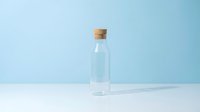 Empty glass bottle with cork stopper on clean white surface against soft blue background for minimalist product photography and packaging design.