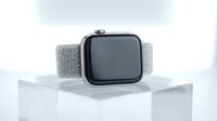 Modern smartwatch with silver mesh band displayed on white cube against clean background for technology and wearable device presentations.