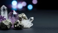 Collection of healing crystals and gemstones including clear quartz, amethyst and pyrite arranged on dark surface with colorful bokeh lights background.