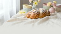 Fresh baked croissants on white linen with pastel Easter eggs and spring flowers in soft natural light for holiday breakfast and bakery concepts.