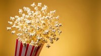 Freshly popped popcorn overflowing from red striped container against warm golden background for movie theater snacks and entertainment concepts.