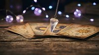 Crystal pendulum hovering over vintage tarot cards with mystical bokeh lights creating magical fortune telling atmosphere for spiritual guidance sessions.