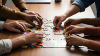 Group of diverse hands working together on jigsaw puzzle pieces on wooden table, teamwork and collaboration concept for business and problem solving.