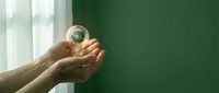 Hands gently holding small Earth globe in protective gesture against green background symbolizing environmental care and global responsibility.