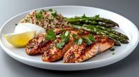 Grilled salmon fillets with mustard-herb crust served alongside quinoa and fresh asparagus spears on white plate, garnished with lemon wedge and parsley.