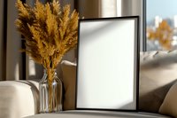 Empty black frame mockup with golden dried pampas grass bouquet in glass vase on table, natural sunlight casting soft shadows, modern home decor.