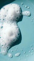 White foam bubbles floating on turquoise water surface with droplets for spa wellness skincare and cleaning product concepts.