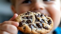 Closeup of a young child's hand holding a freshly baked chocolate chip cookie, perfect for food, parenting, and lifestyle content.